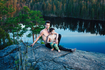 middle age man with little cute son doing sport yoga on the top of the mountain together, happy family lifestyle people outdoor, summer wild nature for training