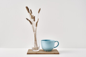 A vase with dry spikelets and a mug stand on a wooden stand on a white background. Minimalism, eco-materials in the interior decor. Copy space, mock up.