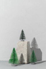 Conceptual festive card with trendy stone podium and three miniature Christmas trees on gray background
