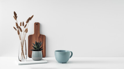 A mug, a potted houseplant, a clear vase and a wooden cutting board. Eco-friendly materials in the decor of the room, minimalism. Copy space, mock up
