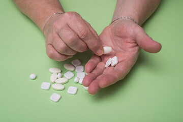 Closeup of woman taking drug pills in hands on green background