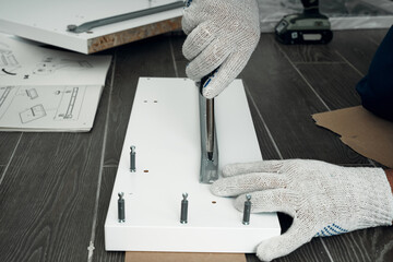 Furniture assembly process. Worker in overalls and white footwear. Using a screwdriver. Do it yourself.