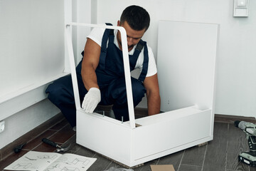 Furniture assembly process. Worker in overalls and white footwear. Joining pieces of furniture. Do...