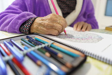 Mujer blanca de noventa años en confinamiento por coronavirus o covid-19, haciendo tareas de dibujo como entretenimiento.
