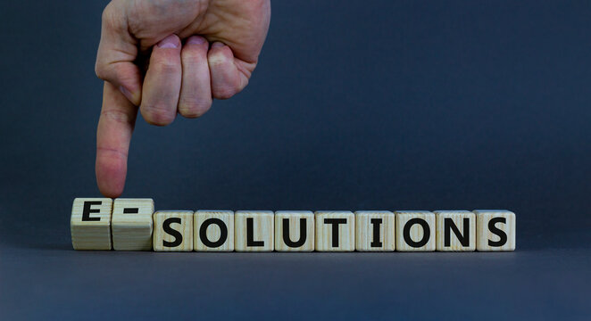 Time to e-solutions. Male hand flips wooden cubes and changes the word 'solutions' to 'e-solutions'. Beautiful grey background, copy space. Business and e-solutions concept.