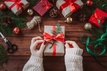 Fototapeta na wymiar Christmas gift wrapping process. Woman decorates box with red ribbon.