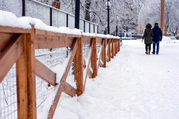 The wooden fences in the park are covered with beautiful fluffy snow. Winter in the city, selective focus.