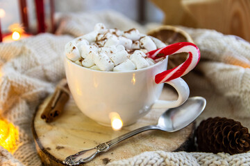 Close-up white cup with coffee and marshmallows, lollipop. Around the plaid, garland. The concept of comfort, hygge.