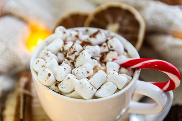 Close-up white cup with coffee and marshmallows, lollipop. Around the plaid, garland. The concept of comfort, hygge.