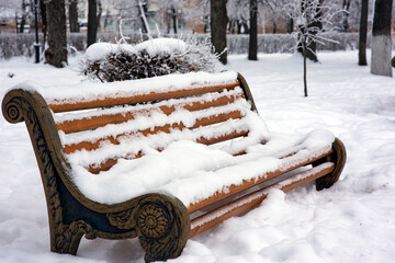 The wooden bench in the park is covered with beautiful fluffy snow. Winter in the city, selective focus, close-up.