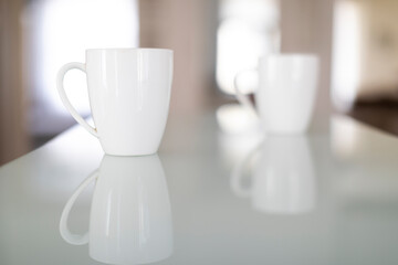 Two white coffee mugs on a reflective glass surface