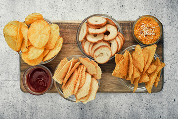 Mix of chips, snacks and crackers on a wooden stand. Unhealthy food, beer snack, ready meal. Close Up