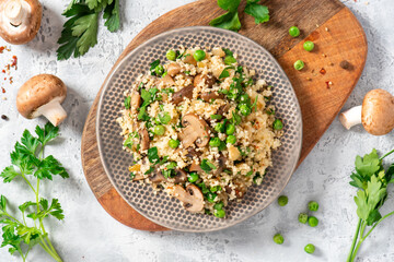 Couscous with fried mushrooms, onions, green peas, and parsley in a plate on a grey background top view. Tasty vegan couscous salad with champignons.