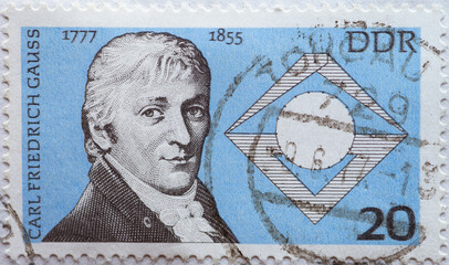 a postage stamp from Germany, GDR showing a portrait of Carl Friedrich Gauß (1777–1855), mathematician, astronomer and physicist, as well as a seventeenth corner with compass and isosceles triangle.