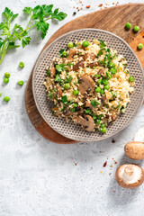 Couscous with fried mushrooms, onions, green peas, and parsley in a plate on a grey background top view. Copy space for text. Tasty vegan couscous salad with champignons.