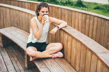 Attractive woman after running drinking coffee or tea and relaxing. Resting Runner.