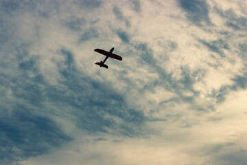 Children's plane on cloudy sky background. Flight of toy plane in the sky. Silhouette of airplane flying in the blue sky.