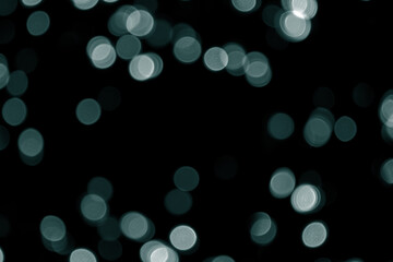 Defocused bokeh christmas green lights on black background. Green bokeh glitter wallpaper for Christmas, New year background. Tidewater Green colors. Abstract blurred green glitter texture.