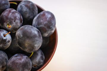 Several ripe blue plums in a deep clay plate on a white background with a copy space