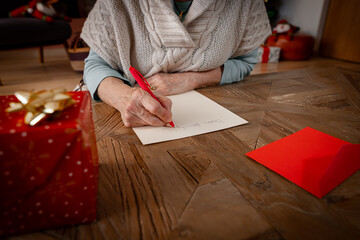 Close up of senior woman's hand writing a letter on yellow paper on wooden table, to her family for...