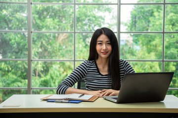 Happy young Asian woman smiling while using laptop in living room by working from home concept with copy space