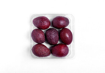 Seven purple avocados in the transparent box on the white table