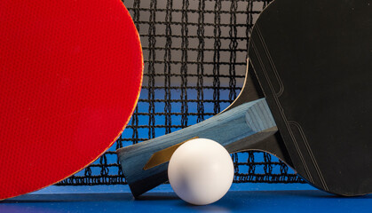 Ping pong rackets and balls on a blue table with net.