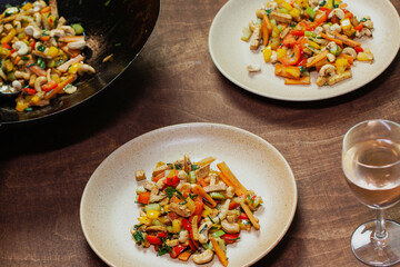 Stir-fry wok dish of cashew nuts, tofu, carrot, vegetables and spices. Ready meal on two plates and glass of rose wine.
