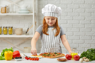 little girl in chef hat and an apron cooking pizza in the kitchen.