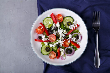 Light plate of Greek salad on a blue napkin on a concrete background.