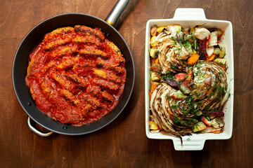Oven baked vegetables with dill in ceramic dish and meat and cabbage rolls in tomato sauce on frying pan.Homemade food  flat lay.