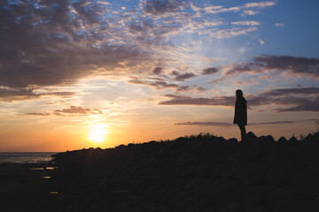 Naklejka na ściany i meble sunset on the beach with rocks and sea and silhouette of a woman