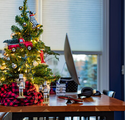 Stand up desk with computer near sunny window decorated with Christmas tree, nutcrackers, bright red ornaments. 