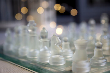 Transparent glass chess pieces on a white wooden table.