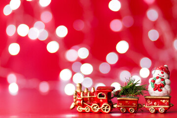 Fototapeta na wymiar Toy steam train with christmas tree and snowman on red background with bokeh