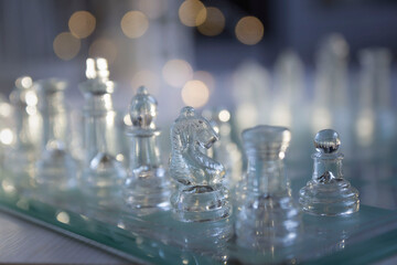 Transparent glass chess pieces on a white wooden table.