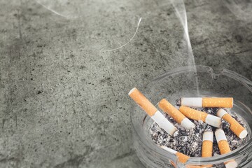 Ashtray and smoked cigarettes with smoke on desk
