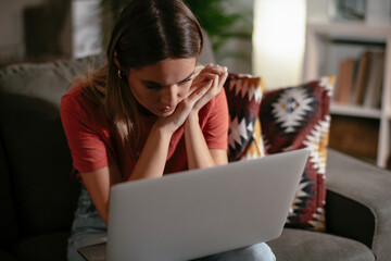 Worried woman using laptop. Young sad woman sitting in the living room.