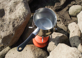Turk with water boils on a portable gas stove among stones