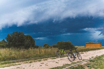 Obraz premium storm clouds over the field with bicycles on a gravel road