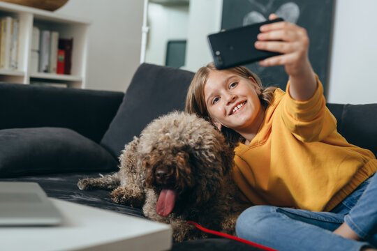 teenage girl sitting on sofa at home with her dog and taking picture with smartphone