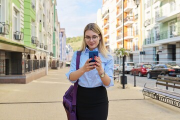 Young business woman with smartphone walking along city street