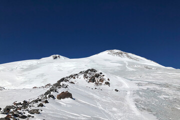Fototapeta na wymiar two peaks of famous Elbrus mountain in Caucasus in winter and background of deep blue sky. The highest european mountain is attractive for aplinists.