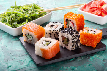 Assorted rolls on a colored background with ginger and Chuka salad.