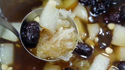 A ladle scooping up some healthy Chinese dessert of snow fungus and pear sweet soup, with also red dates and lotus seeds.