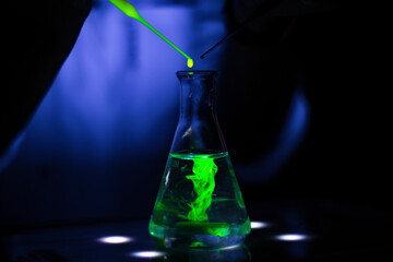  European researcher working with a green fluorescent compound in dark chemistry laboratory for...