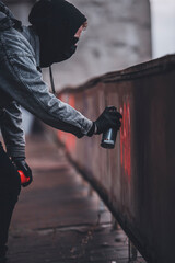 Close shoot of Young anonymous graffitist making protest graffiti with red spray paint