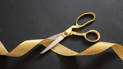 Grand opening. Gold scissors cutting gold satin ribbon, black background