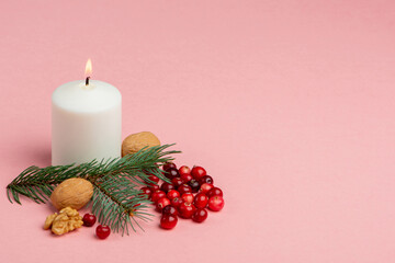 Christmas composition with white candle, spruce twig, walnuts and cranberries on a pink background.