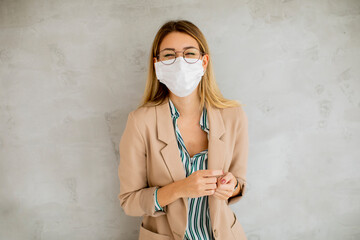Young woman standning by the grey wall and wearing a respiratory mask from coronavirus disease